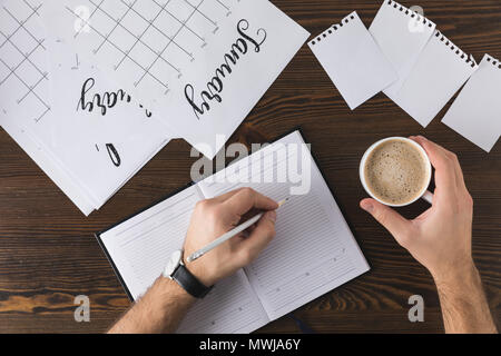 partial view of businessman making notes in notebook at table with calendar Stock Photo