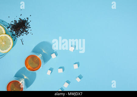 top view of fresh tea in cups, sugar cubes, dry herbal tea and sliced lemon on blue Stock Photo