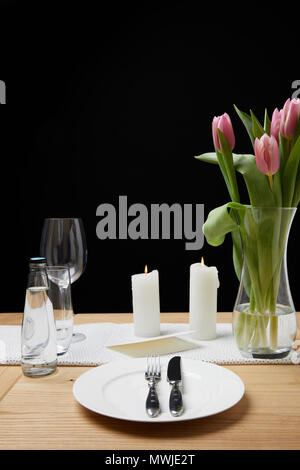 Vase with flower bouquet and candles on table with festive tableware Stock Photo