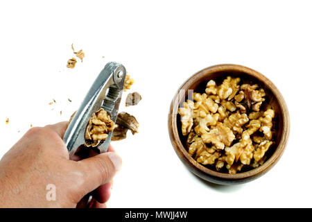 Man hand is cracking a walnut with metal nutcracker and kernel walnuts in wooden bowl on isolated white background Stock Photo