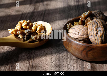 Whole walnuts and kernel walnuts in wooden bowl and wooden spoon on dark walnut table background Stock Photo
