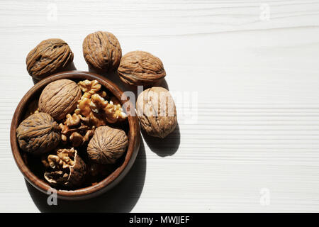 Kernel walnuts in wooden bowl with whole walnuts on white wooden table background Stock Photo
