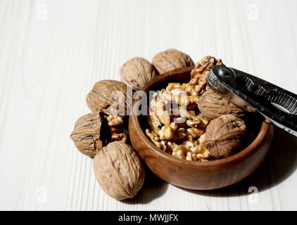 Kernel walnuts in wooden bowl with whole walnuts and nutcracker on white wooden table background Stock Photo