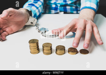 There are gold coins on the table, the man freed himself from the cuffs and reaches for the coins. Machle financial, financial problems, financial pyr Stock Photo