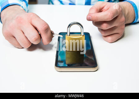 The man is holding a key to the padlock under the mobile phone. The concept of securing the phone, cyber attack, data security problems on a personal  Stock Photo