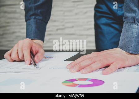 Businessman analyzing on wooden desk at the office. The man is holding a pen leaning over the reports and graphs. Expenses and profits. Balance of cos Stock Photo