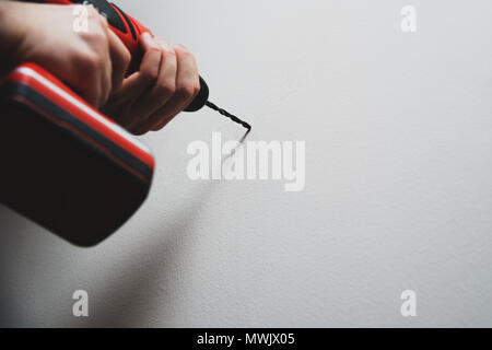 Drilling in the wall. The man is holding a screwdriver or drill in hand. Drills a hole in the wall using a drill with a drill. Concept of housework, r Stock Photo