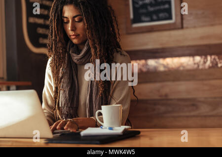 Woman sitting in a restaurant working on laptop. Freelancer sitting in cafe with a coffee and notepad working on laptop computer. Stock Photo