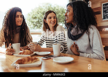 Three women sitting and talking in a restaurant. Friends sitting in a cafe with coffee and snacks on the table and discussing. Stock Photo