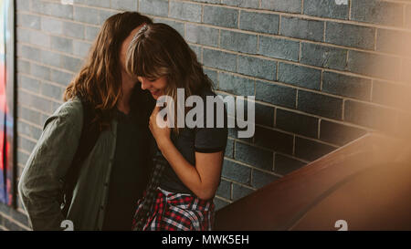 university couple in love standing on stairs and smiling. Young man whispering something funny to his girlfriend in high school. Stock Photo