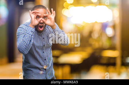 African american man with beard looking at camera through fingers in ok gesture. Imitating binoculars at night Stock Photo