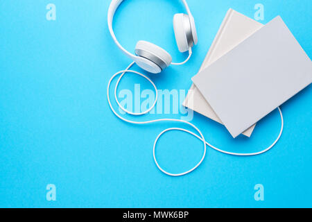 Top view of white headphones and notebooks on blue background with copy space. Flat lay. Stock Photo