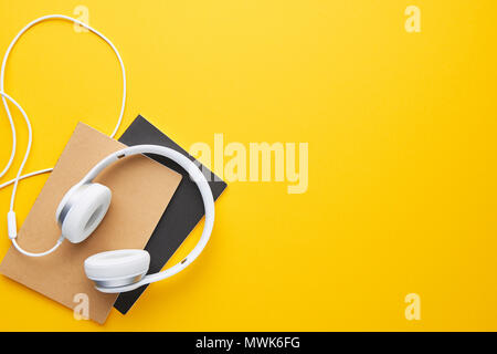 Top view of white headphones and notebooks on yellow background with copy space. Flat lay. Stock Photo