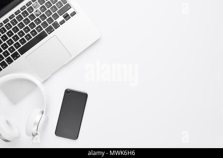 Minimal work space concept. Top view of laptop, white headphones and black cell phone on white background with copy space. Flat lay. Stock Photo
