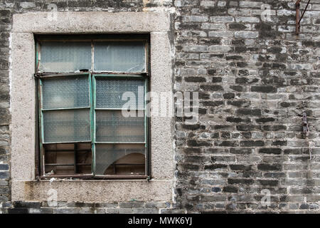 Old rough gray bricks wall with dirty broken glass window. Building facade. Stock Photo