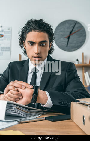 portrait of surprised businessman checking time on watch while sitting at workplace in office Stock Photo