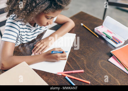 Little girl sitting at the table and writing in her notebook Stock Photo