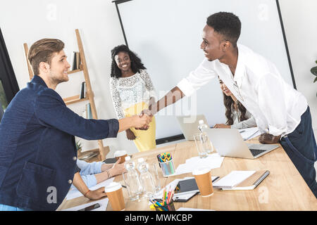 side view of multiethnic business partners shaking hands at meeting in conference room Stock Photo