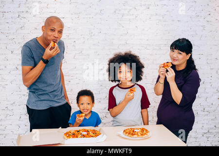 Happy family of African American parents and little boy and girl having pizza together happily at home. Family and parenthood concept Stock Photo