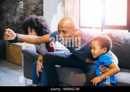 Happy African American family of three watching tv and cheering sport games on sofa at home Stock Photo