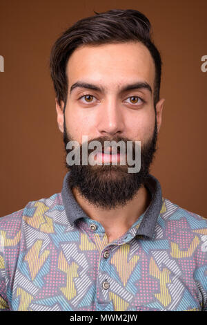 Young handsome bearded Persian man against brown background Stock Photo