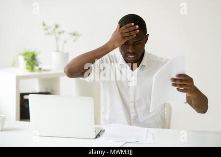 Frustrated African American looking at mistakes in papers Stock Photo