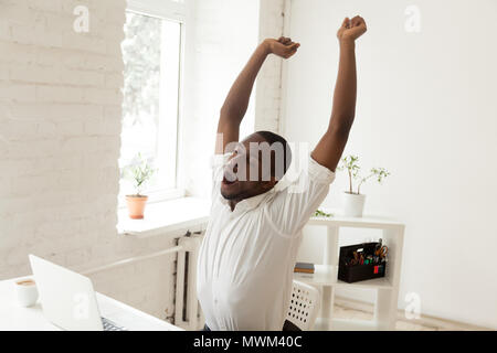 Tired black worker yawning and stretching in office chair Stock Photo
