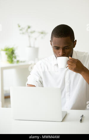 Focused black worker drinking coffee checking emails in office Stock Photo