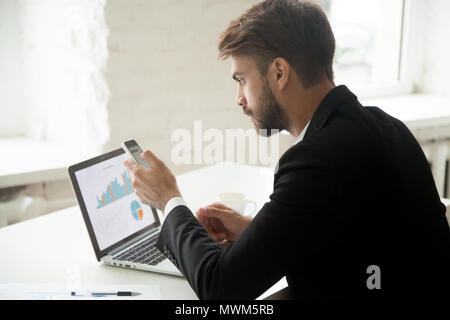 Serious entrepreneur writing email on cellphone while working at Stock Photo