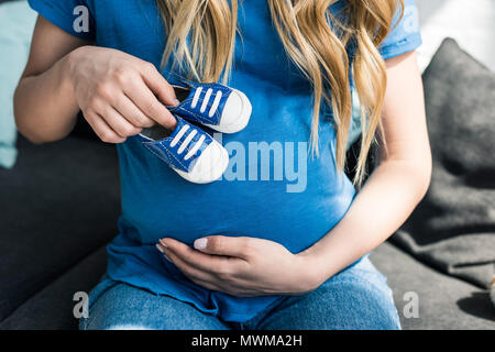 cropped image of pregnant woman touching belly with baby shoes Stock Photo
