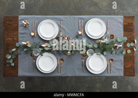 top view of rustic table setting with eucalyptus, tarnished cutlery, wine glasses, candles and empty plates on tabletop Stock Photo