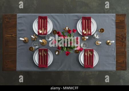 top view of rustic table setting with red tulips bouquet, tarnished cutlery, wine glasses, candles and empty plates on tabletop Stock Photo