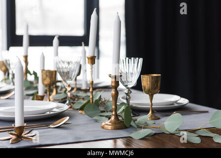 rustic table arrangement with eucalyptus, vintage cutlery, candles in candle holders and empty plates Stock Photo