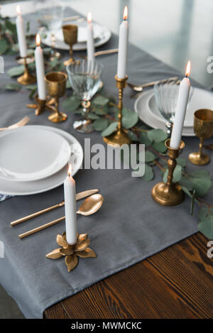 close up view of rustic table arrangement with eucalyptus, vintage cutlery, candles in candle holders and empty plates Stock Photo