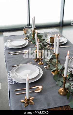 close up view of rustic table arrangement with eucalyptus, vintage cutlery, candles in candle holders and empty plates Stock Photo