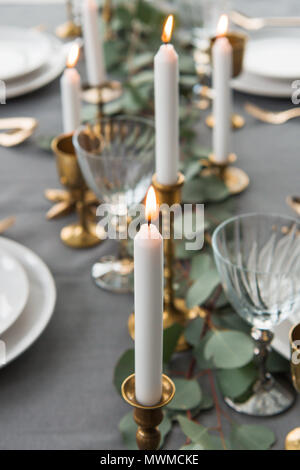 selective focus of rustic table setting with eucalyptus, old fashioned cutlery, candles in candle holders and empty plates Stock Photo