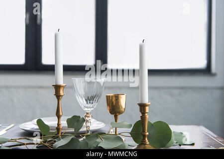 close up view of rustic table arrangement with wine glasses, eucalyptus, candles in vintage candle holders and empty plates Stock Photo