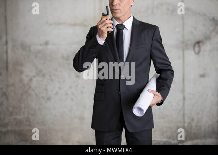 Cropped shot of engineer in formal wear holding blueprint and using walkie-talkie Stock Photo