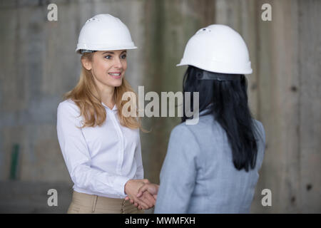Two professional engineers in hard hats shaking hands and looking at each other Stock Photo