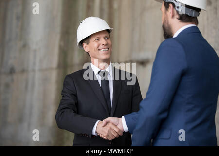 Two professional engineers in hard hats shaking hands and looking at each other Stock Photo