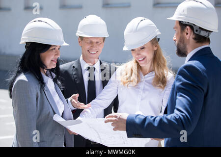 Professional team of smiling architects in hard hats working together with blueprint Stock Photo