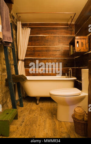 Bathroom with white porcelain claw foot bathtub and high back toilet inside an old circa 1850 cottage style fieldstone home Stock Photo