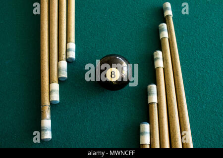 Eight ball billiard in the middle of a group of cues on a green table Stock Photo