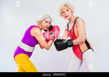 side view of senior sportswomen in boxing gloves training and looking at camera isolated on grey Stock Photo