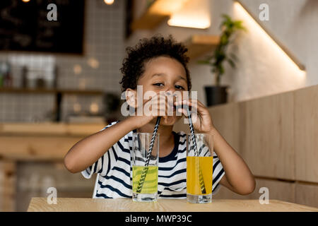 cute african american boy drinking juice from two glasses and looking at camera Stock Photo