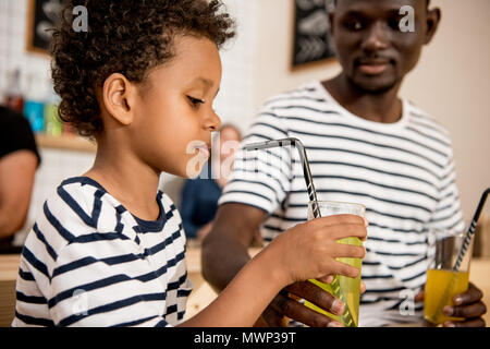 cute african american boy drinking lemonade while sitting with father in cafe Stock Photo