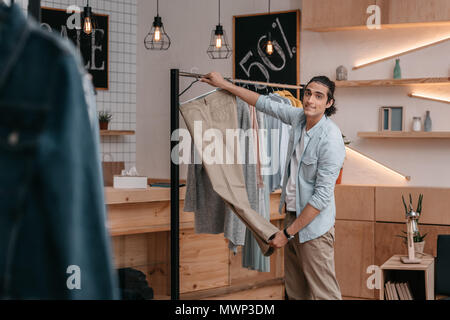 handsome young business owner hanging and selecting clothes before opening in boutique Stock Photo