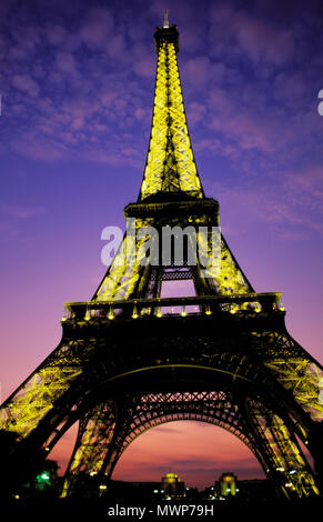 Eiffel Tower, close view on Champ de Mars looking up at dusk, depicting lights on a with little fluffy clouds and twilight glow, Paris, France Stock Photo