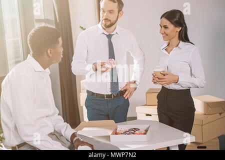 smiling multiethnic colleagues talking and looking at each other during coffee break in new office Stock Photo