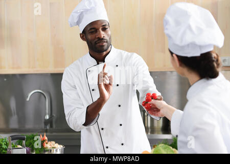 African american chef and female cook sharing cooking ingredients on kitchen Stock Photo